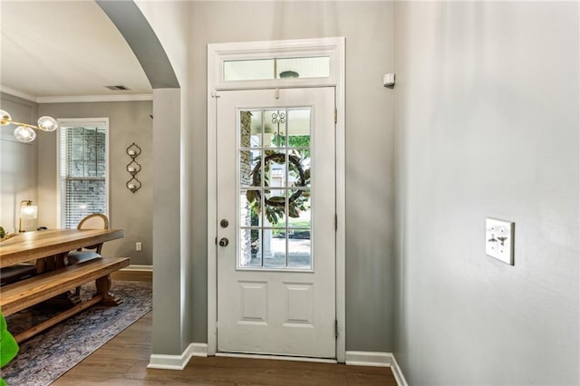 entryway with crown molding, arched walkways, baseboards, wood finished floors, and visible vents