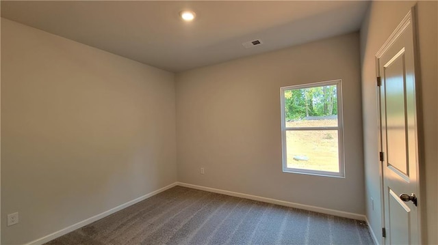 spare room featuring dark colored carpet, visible vents, and baseboards