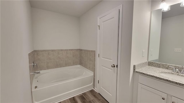 bathroom with a garden tub, wood finished floors, and vanity