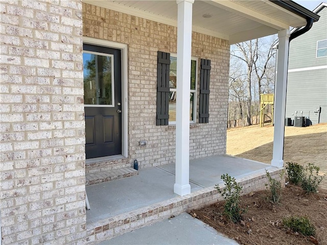 entrance to property featuring central air condition unit, brick siding, and covered porch