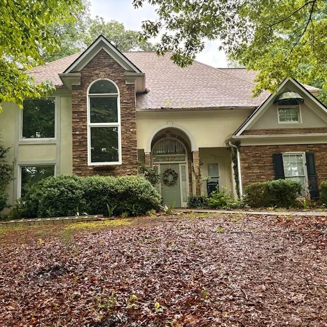 view of front of home featuring a shingled roof, stucco siding, and stone siding