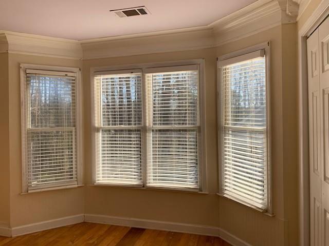 empty room featuring light wood-type flooring, baseboards, plenty of natural light, and crown molding