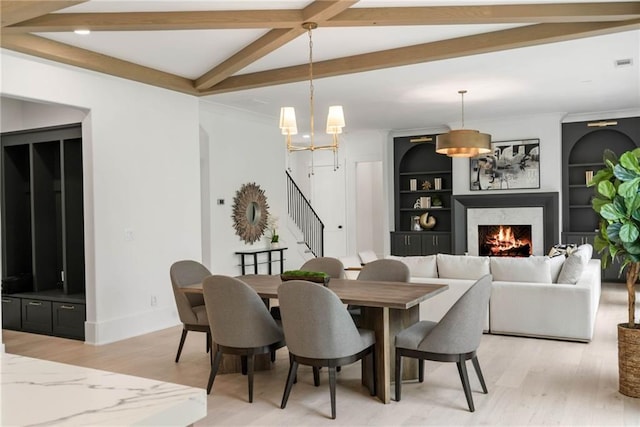 dining area featuring light hardwood / wood-style floors, a high end fireplace, built in features, and beamed ceiling