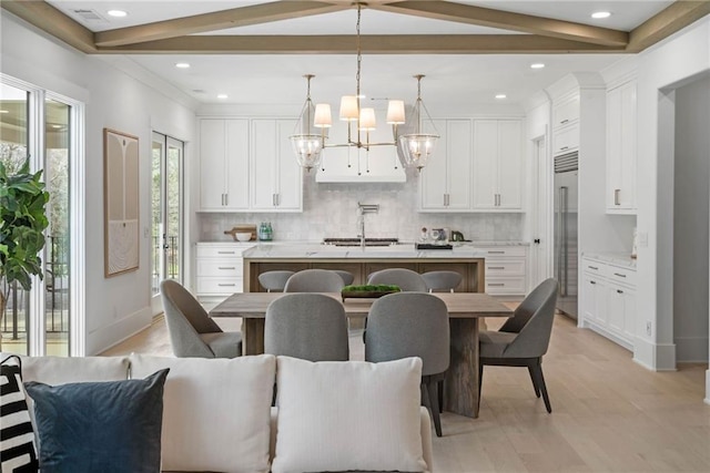 kitchen with white cabinetry, sink, hanging light fixtures, a kitchen island with sink, and light hardwood / wood-style flooring