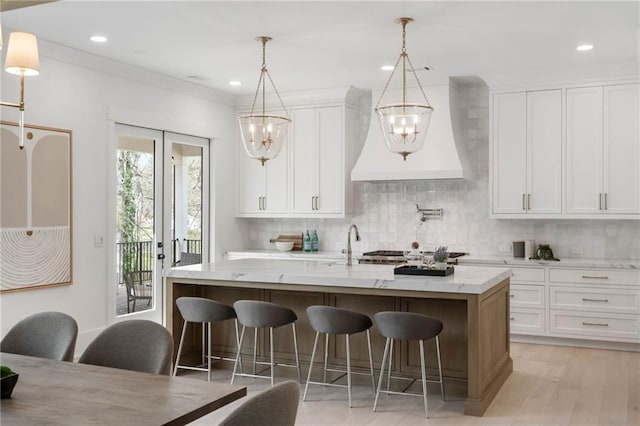 kitchen with light stone counters, white cabinetry, and a kitchen island with sink