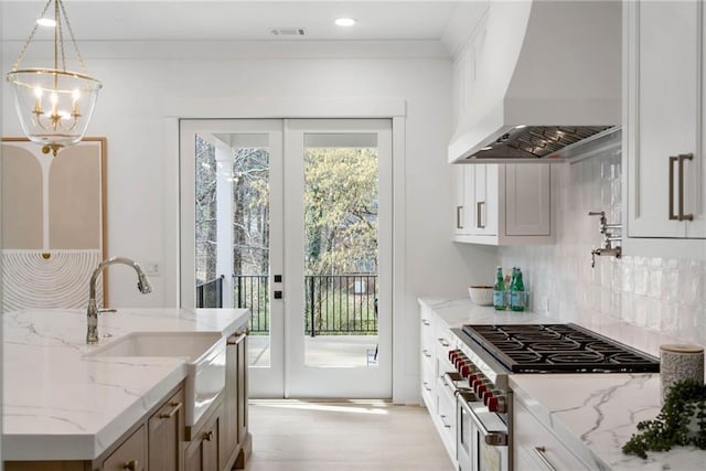 kitchen with high end stove, sink, hanging light fixtures, custom range hood, and light stone counters