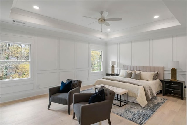 bedroom with light wood-type flooring, ceiling fan, and a raised ceiling