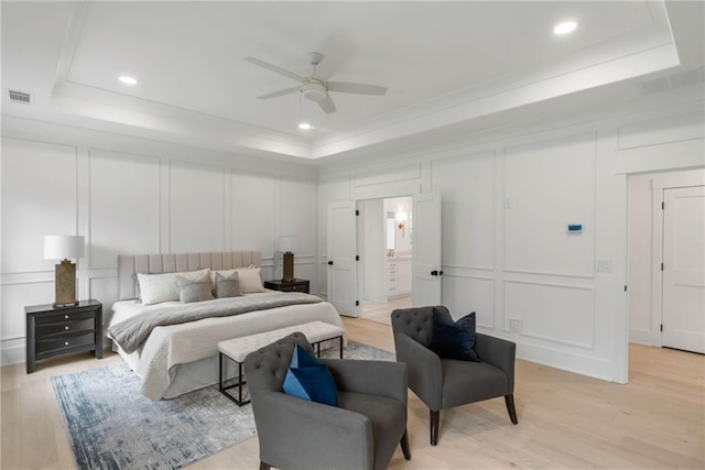 bedroom with ceiling fan, light hardwood / wood-style floors, ensuite bath, and a raised ceiling