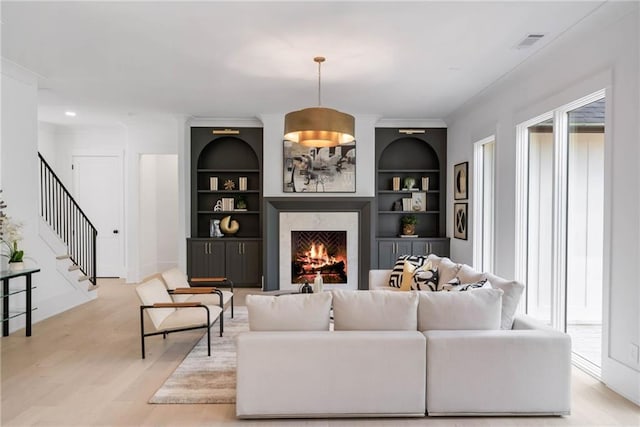 living room featuring light wood-type flooring, a fireplace, and built in shelves