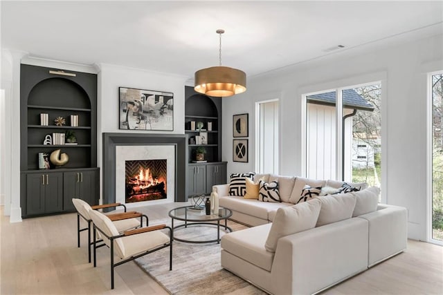 living room with light wood-type flooring, built in features, a premium fireplace, and crown molding