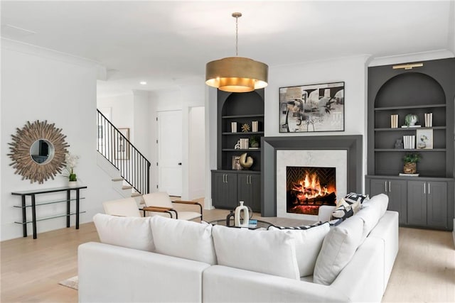 living room featuring light hardwood / wood-style floors, built in features, crown molding, and a fireplace