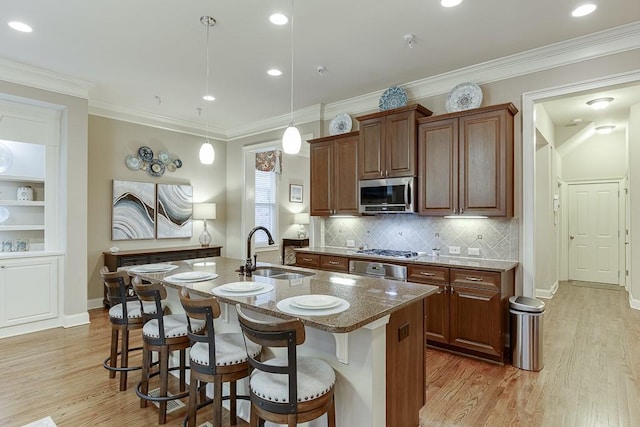 kitchen featuring a breakfast bar area, stone countertops, a sink, stainless steel appliances, and light wood-style floors