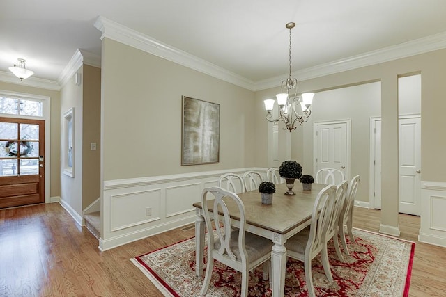 dining room featuring a decorative wall, an inviting chandelier, crown molding, and light wood finished floors