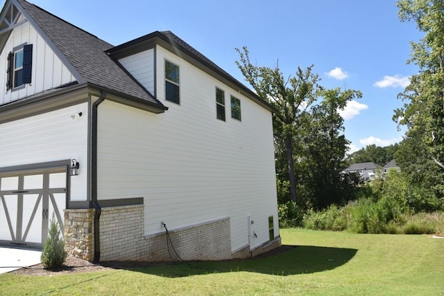 view of side of property with brick siding, board and batten siding, roof with shingles, a lawn, and a garage