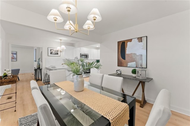 dining room with light wood-type flooring, baseboards, and an inviting chandelier