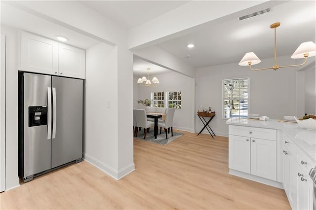 kitchen with light stone counters, stainless steel refrigerator with ice dispenser, visible vents, hanging light fixtures, and white cabinets