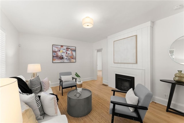 living area with a glass covered fireplace, baseboards, and light wood-style flooring