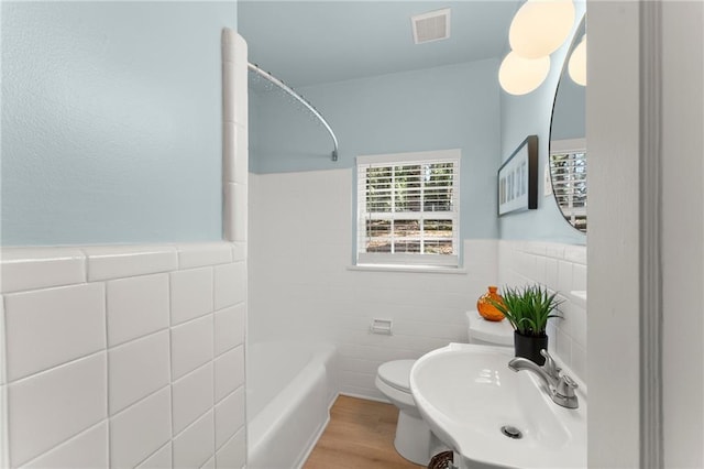 full bathroom with toilet, tile walls, visible vents, and a sink