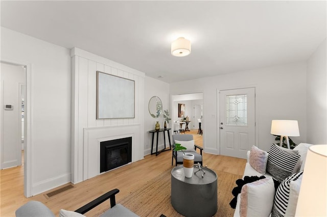 living area with a glass covered fireplace, visible vents, baseboards, and light wood-style flooring