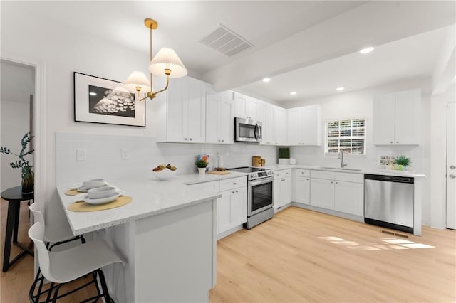 kitchen featuring visible vents, a sink, appliances with stainless steel finishes, a breakfast bar area, and a peninsula