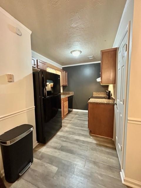 kitchen with brown cabinets, light wood-style flooring, ornamental molding, freestanding refrigerator, and a textured ceiling