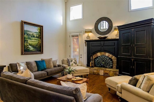 interior space with dark wood-style floors, a stone fireplace, and a towering ceiling