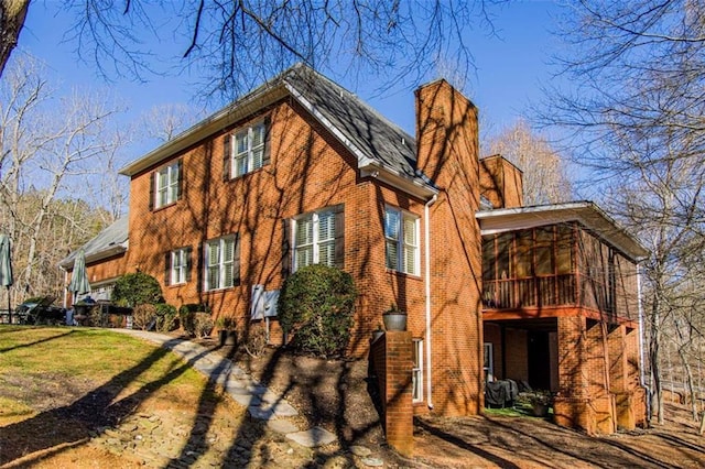 view of home's exterior featuring brick siding, a chimney, and a sunroom