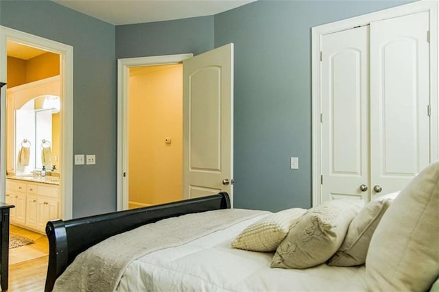 bedroom featuring a closet, ensuite bath, and light wood-style flooring