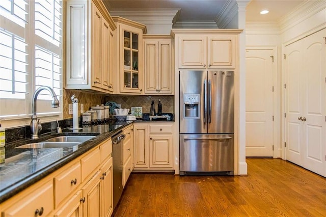 kitchen featuring stainless steel appliances, a sink, ornamental molding, dark stone counters, and glass insert cabinets