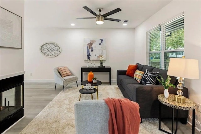 living room with hardwood / wood-style floors, ceiling fan, and a multi sided fireplace