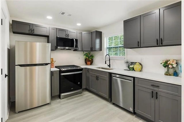 kitchen with gray cabinetry, sink, stainless steel appliances, and light hardwood / wood-style floors