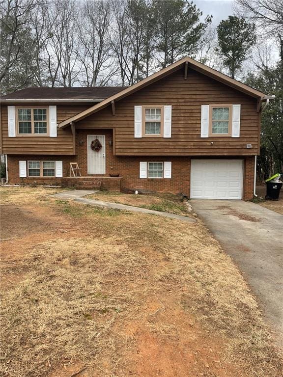 raised ranch with an attached garage, driveway, and brick siding