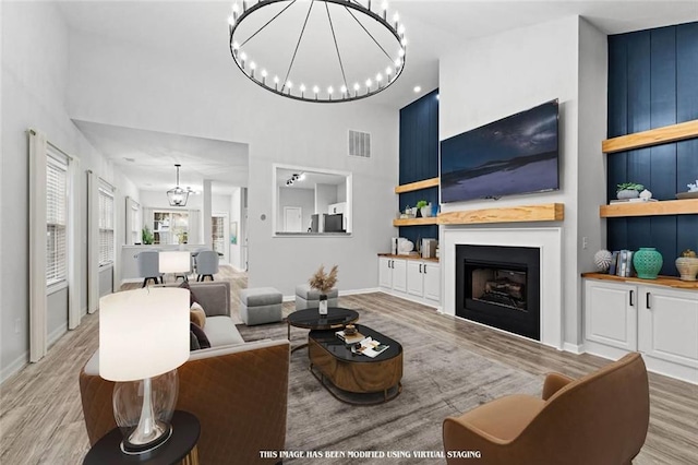 living room with light wood-type flooring, a chandelier, and a towering ceiling