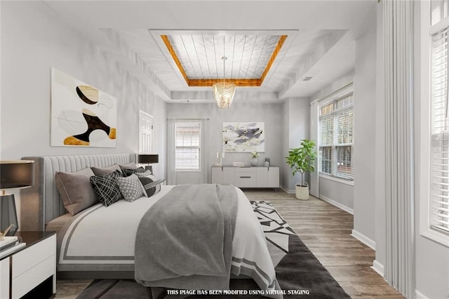 bedroom with hardwood / wood-style flooring, a tray ceiling, and multiple windows