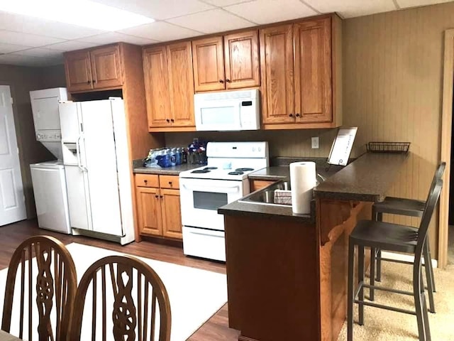 kitchen featuring a breakfast bar area, a paneled ceiling, kitchen peninsula, and white appliances