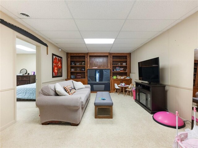 living room with a drop ceiling, carpet flooring, and built in shelves