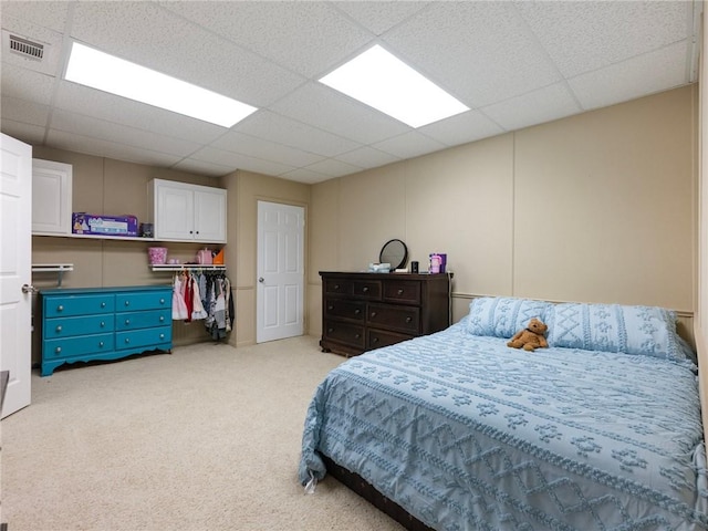 bedroom with light colored carpet, a drop ceiling, and a closet