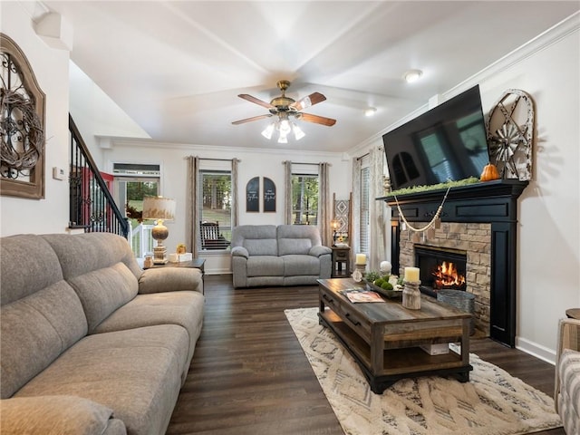 living room featuring ornamental molding, ceiling fan, dark hardwood / wood-style floors, and a stone fireplace