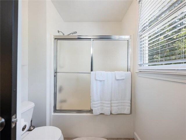 bathroom featuring combined bath / shower with glass door and toilet