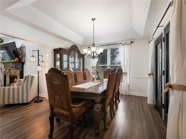 dining area featuring a raised ceiling, a fireplace, dark hardwood / wood-style floors, and a chandelier