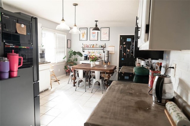 kitchen with white cabinetry, hanging light fixtures, light tile patterned floors, and stainless steel fridge