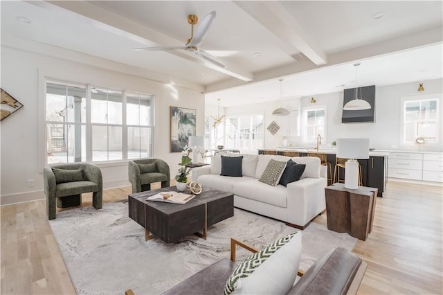 living room featuring sink, ceiling fan, beamed ceiling, and light wood-type flooring