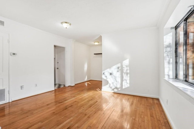 unfurnished room featuring wood-type flooring, visible vents, baseboards, and crown molding