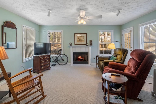 carpeted living room with a tiled fireplace, ceiling fan, and a textured ceiling