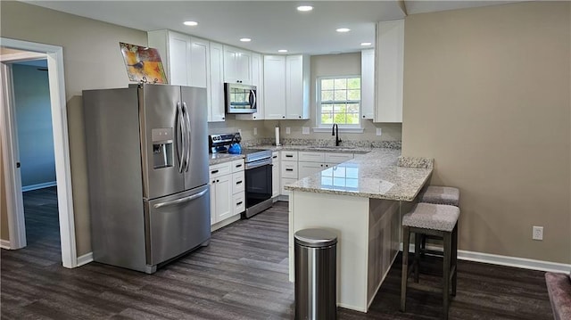 kitchen featuring light stone countertops, a peninsula, white cabinetry, appliances with stainless steel finishes, and a breakfast bar area