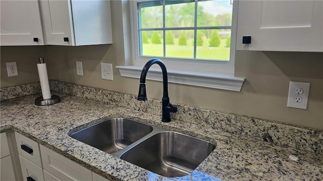 details featuring white cabinets, light stone countertops, and a sink