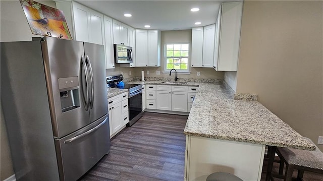 kitchen featuring a peninsula, white cabinetry, appliances with stainless steel finishes, light stone counters, and a sink