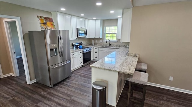 kitchen with a sink, a kitchen breakfast bar, a peninsula, dark wood-style floors, and stainless steel appliances