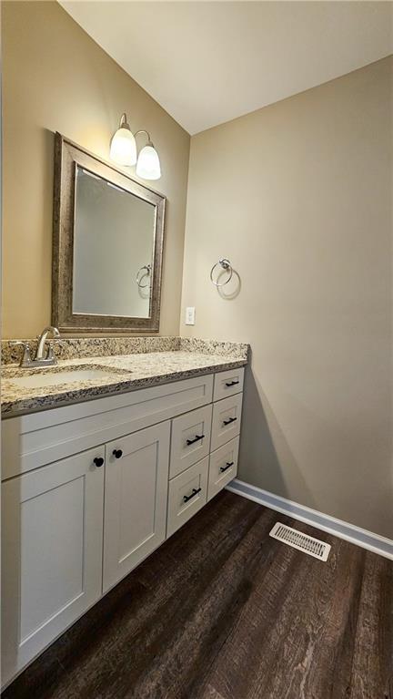 bathroom with vanity, visible vents, baseboards, and wood finished floors