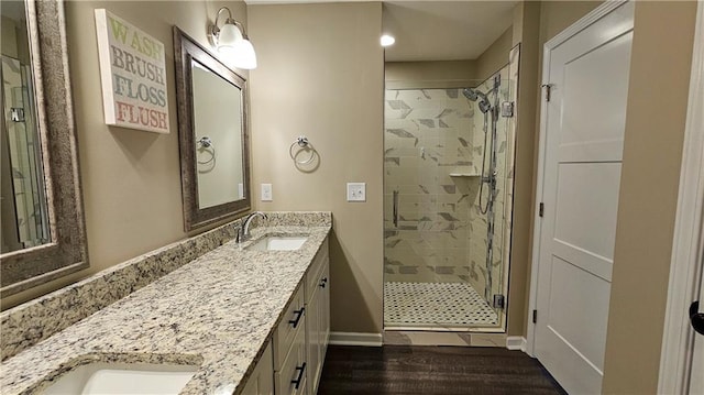 bathroom with a shower stall, double vanity, a sink, and wood finished floors
